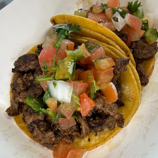 Close-up of grilled beef tacos in corn tortillas, topped with fresh tomato, onion, peppers, cilantro, and lime.