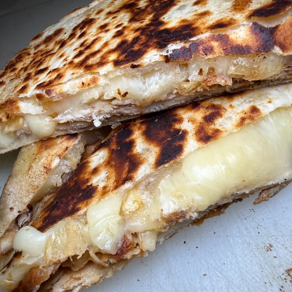 Close-up of a charred, folded flatbread filled with melted cheese and shredded meat.