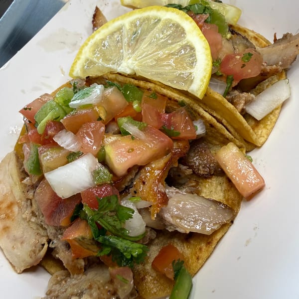 Crispy tacos topped with grilled meat, pico de gallo, cilantro, onion, peppers, and a fresh lemon slice.