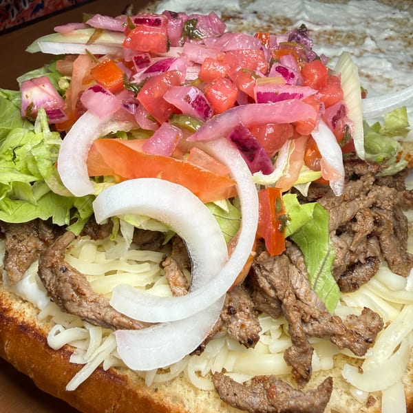 Open sandwich topped with grilled beef, shredded lettuce, tomatoes, onions, pickled vegetables, and creamy sauce.