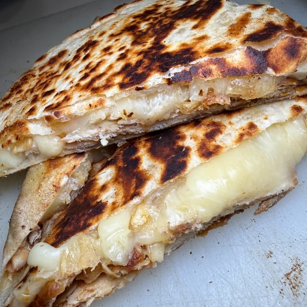 Close-up of golden, charred flatbread layered with melted cheese and a savory filling.